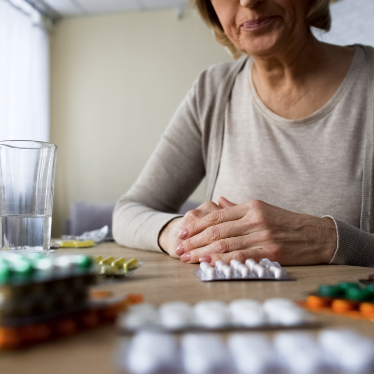 Seniorka siedząca przy stole, na którym leżą opakowania tabletek.
