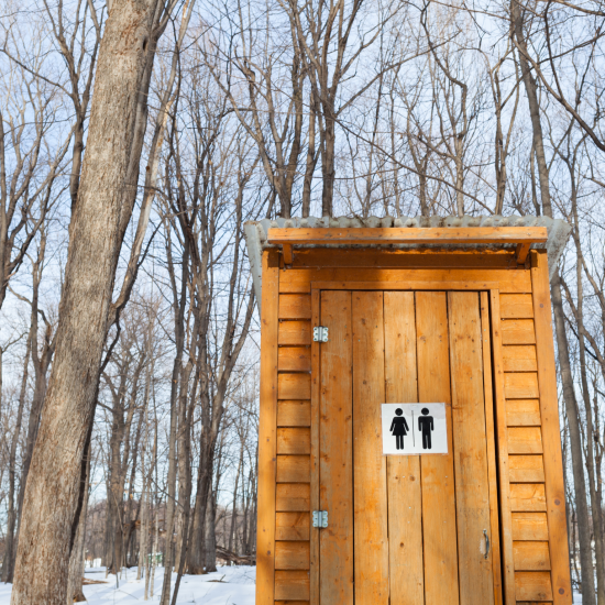 Drewniana toaleta w zimowej leśnej scenerii.