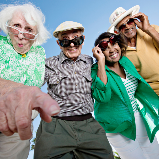 Czterech seniorów: dwie seniorki i dwóch seniorów. Ubrani kolorowo, uśmiechnięci, w okularach przeciwsłonecznych.