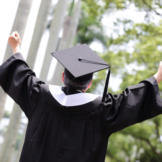 Odwrócony tyłem senior-student ubrany w togę i czapkę absolwenta.