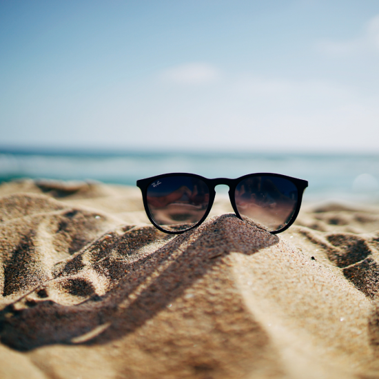 Okulary przeciwsłoneczne leżące na piasku. W tle woda i niebo.