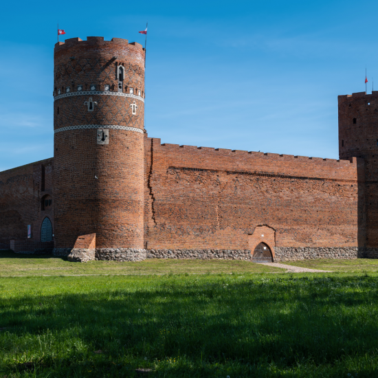 Budynek zamku w Ciechanowie. Błękitne niebo, soczysta, zielona trawa.